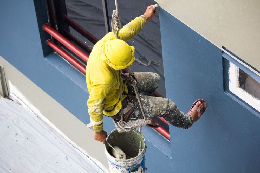 A Man Is Painting A Building With A Bucket Of Paint — L & S Wirth Painting in Dubbo, NSW
