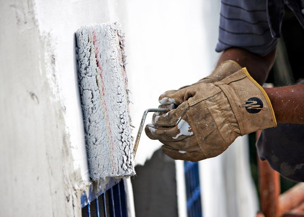 A Man Wearing Gloves Is Painting A Wall With A Paint Roller — L & S Wirth Painting in Dubbo, NSW