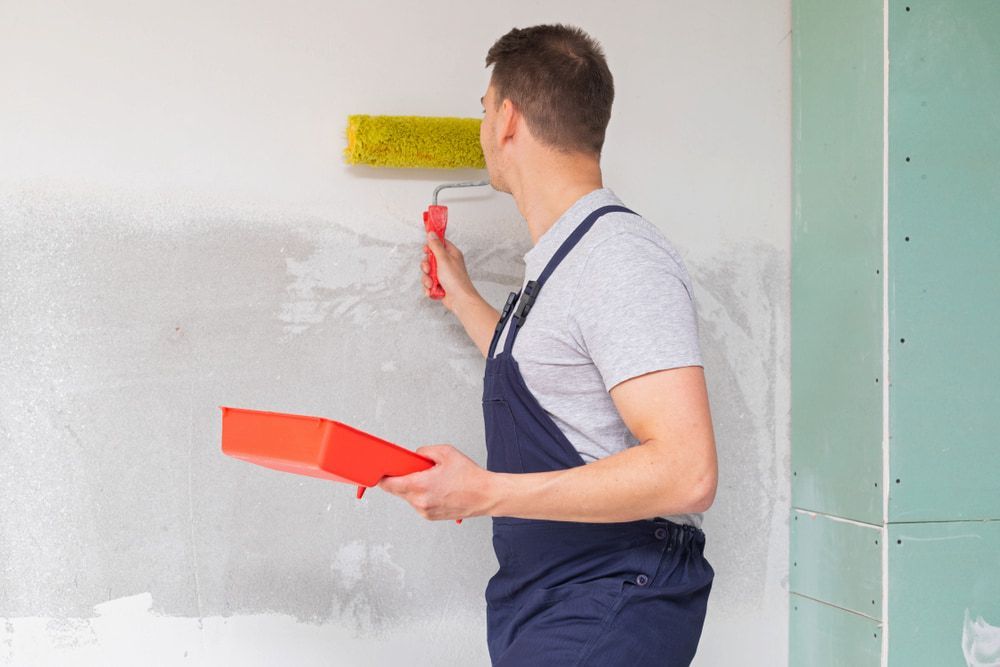 A Man Is Painting A Wall With A Paint Roller — L & S Wirth Painting in Forbes, NSW
