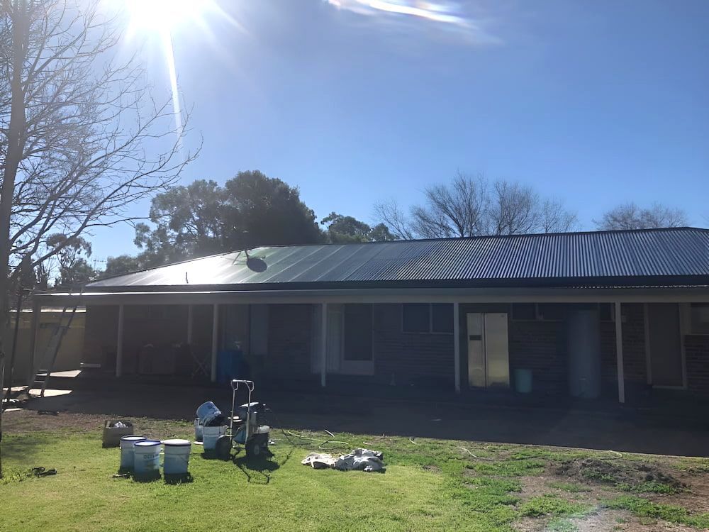 A House With A Black Roof Is Sitting On Top Of A Lush Green Field — L & S Wirth Painting in Dubbo, NSW