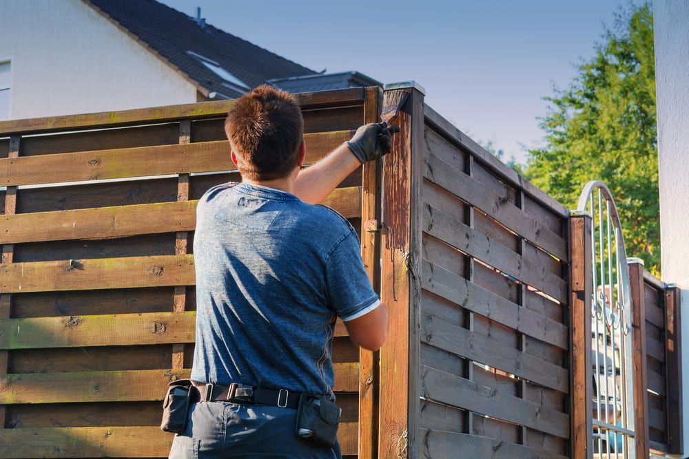 A Man Is Painting A Wooden Fence In Front Of A House — L & S Wirth Painting in Wellington, NSW