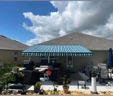 Backyard with a blue and white striped awning over a patio with furniture and a cloudy sky.