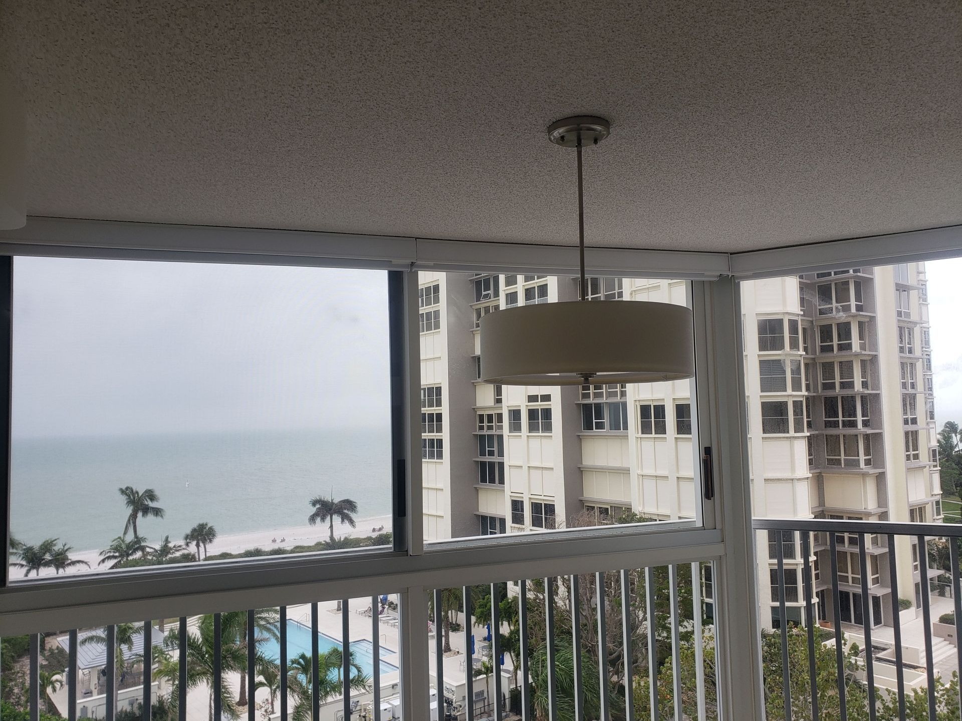 Balcony view of ocean and high-rise buildings on a cloudy day; a light fixture hangs overhead.