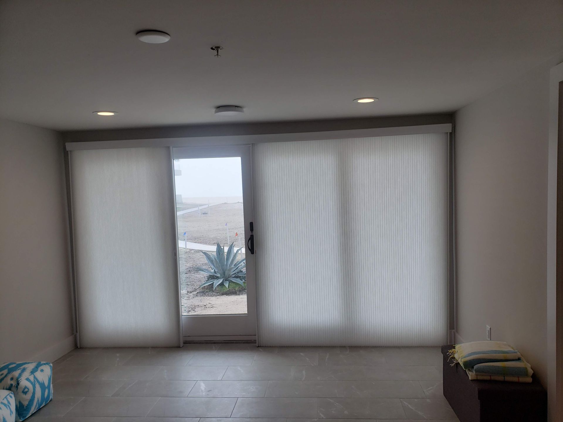 Interior view of a room with light-colored blinds over a sliding glass door looking out onto a landscape.