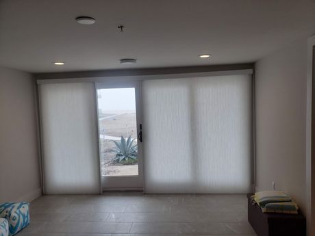 Room with large sliding glass door, sheer white blinds, neutral walls, and outdoor view.
