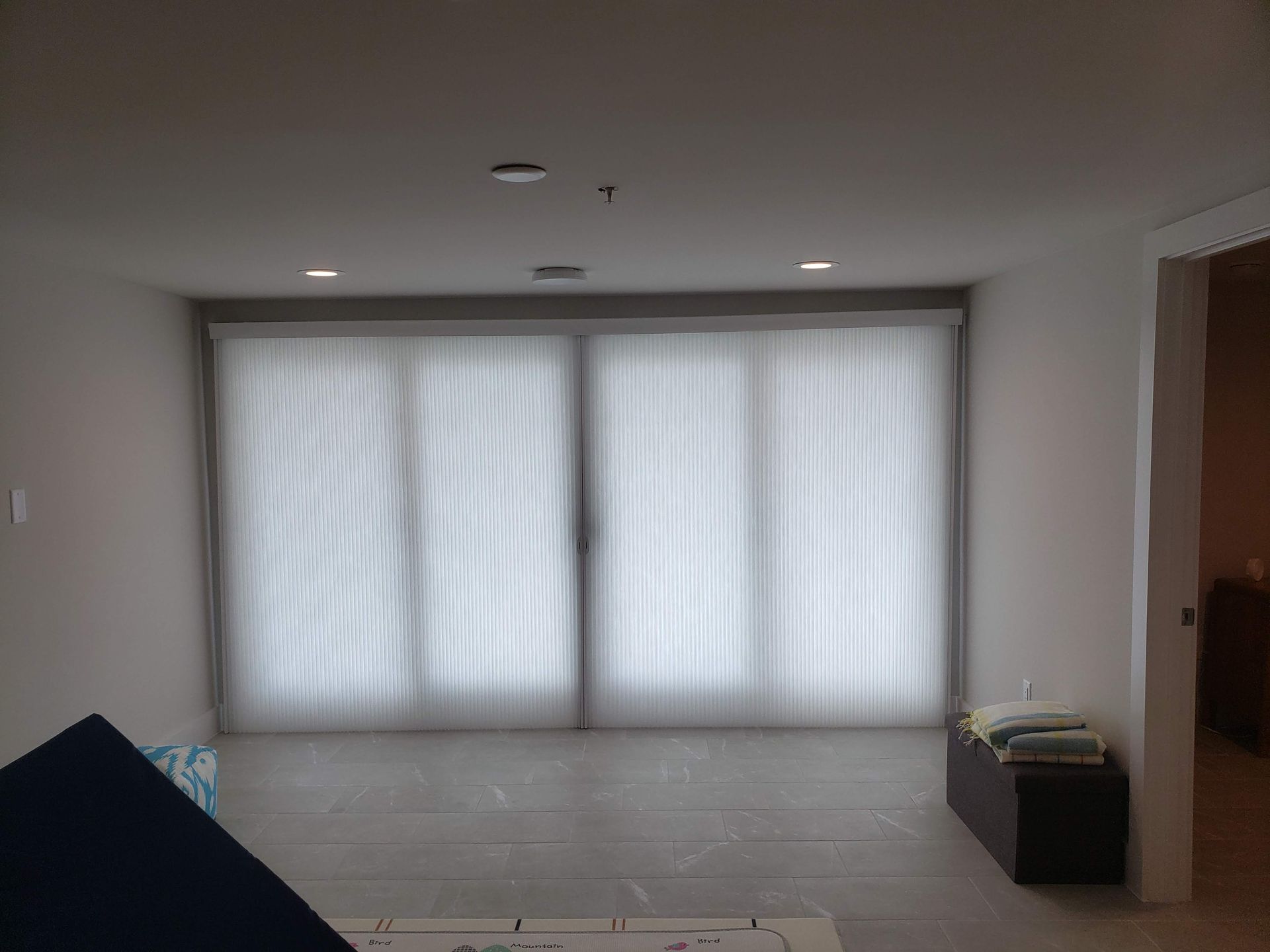 A room with large windows covered by white blinds, open doorway to the right, blue object in foreground.