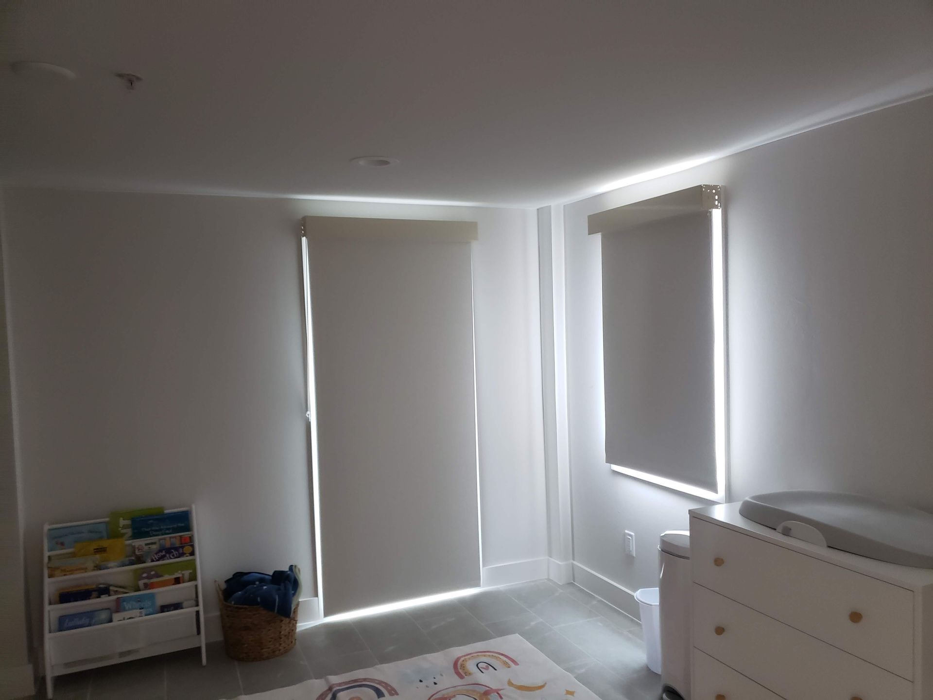 A room with two closed blinds. A bookshelf is on the left, a changing table is on the right.