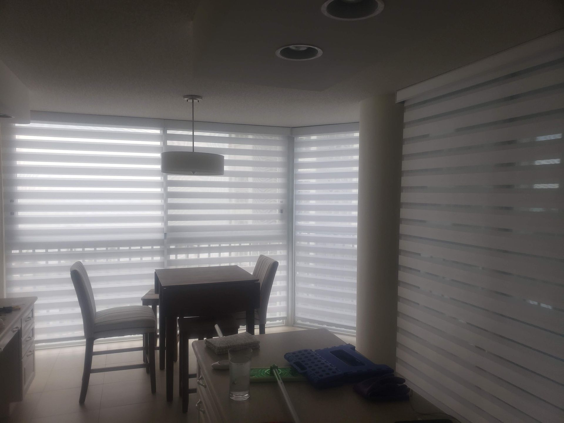 Dining area with white horizontal blinds, table, chairs, and overhead light.