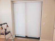 White roller shade over a glass door. A stepladder and power drill are visible.
