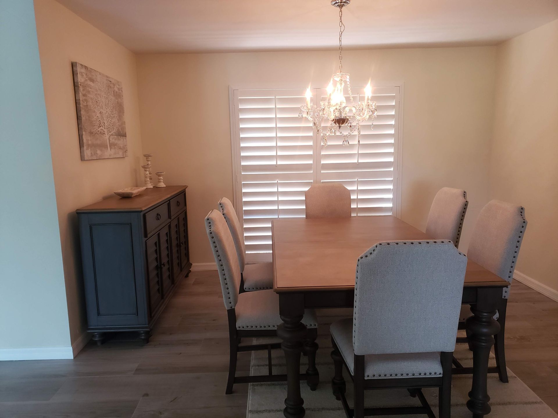 Dining room with a table, chairs, buffet, and chandelier. Shutters on a window.