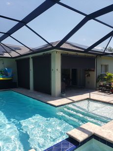 Pool with dark gray shade covers extending from a house under a screen enclosure.