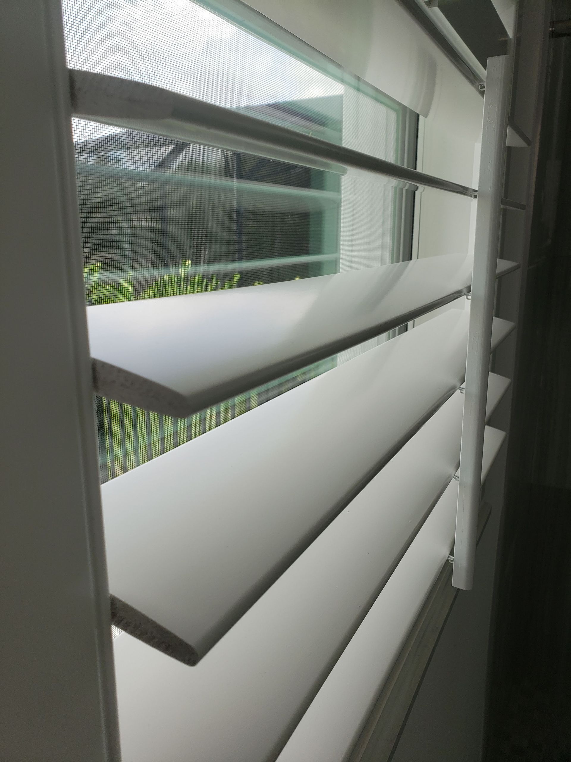 White window shutters partially open, letting in light. View through the shutters to the outside.