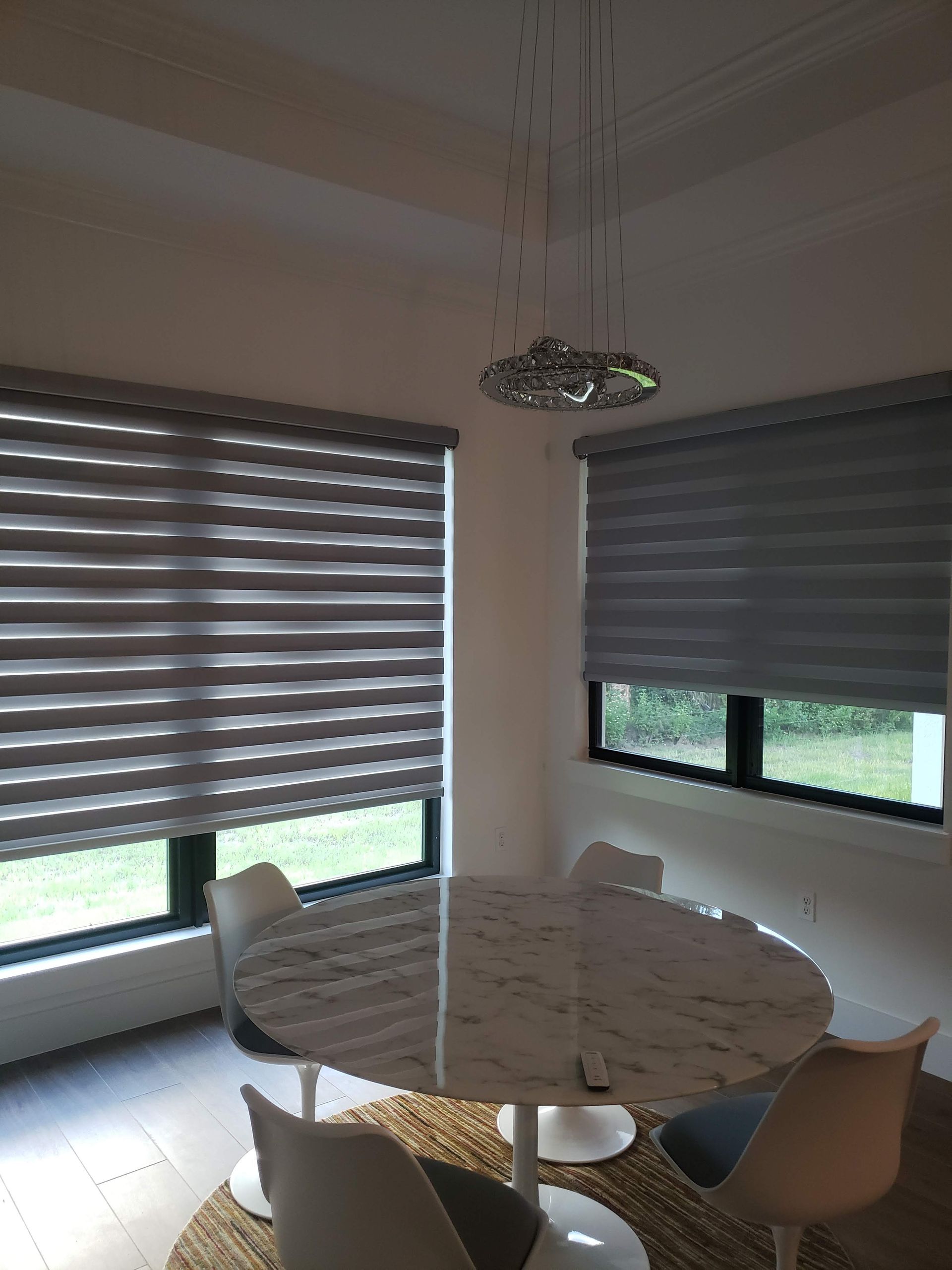 Dining room with round marble table, modern chairs, and layered gray blinds.