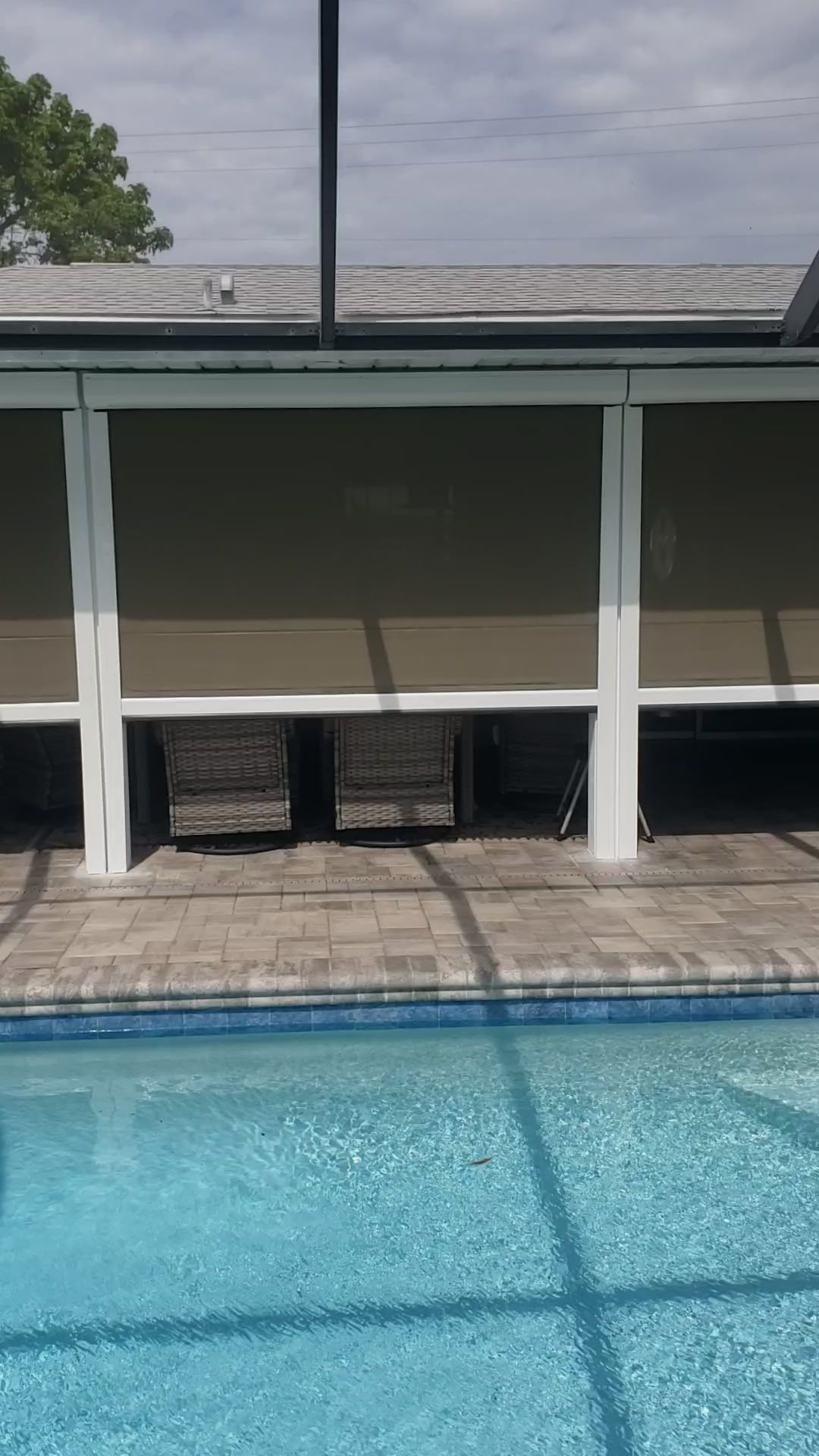 Poolside with outdoor shades. Brown shades are down. Two chairs sit under the shades. Blue pool.