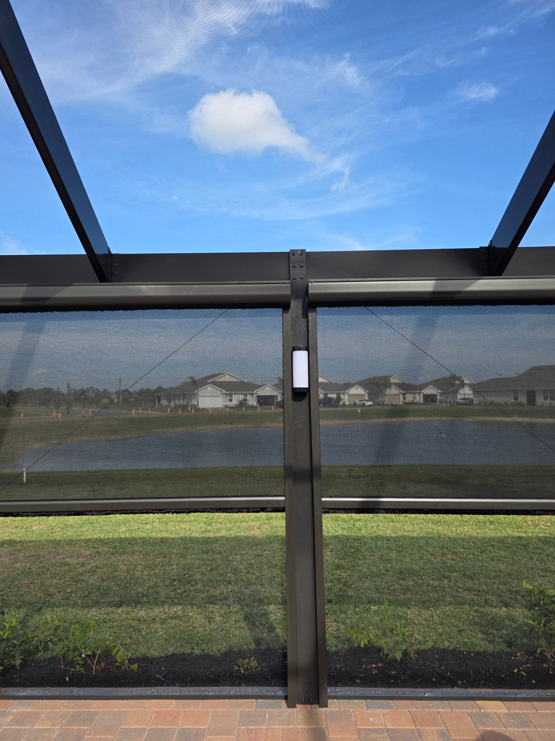 Outdoor patio with a screen overlooking a lake and houses under a blue sky.