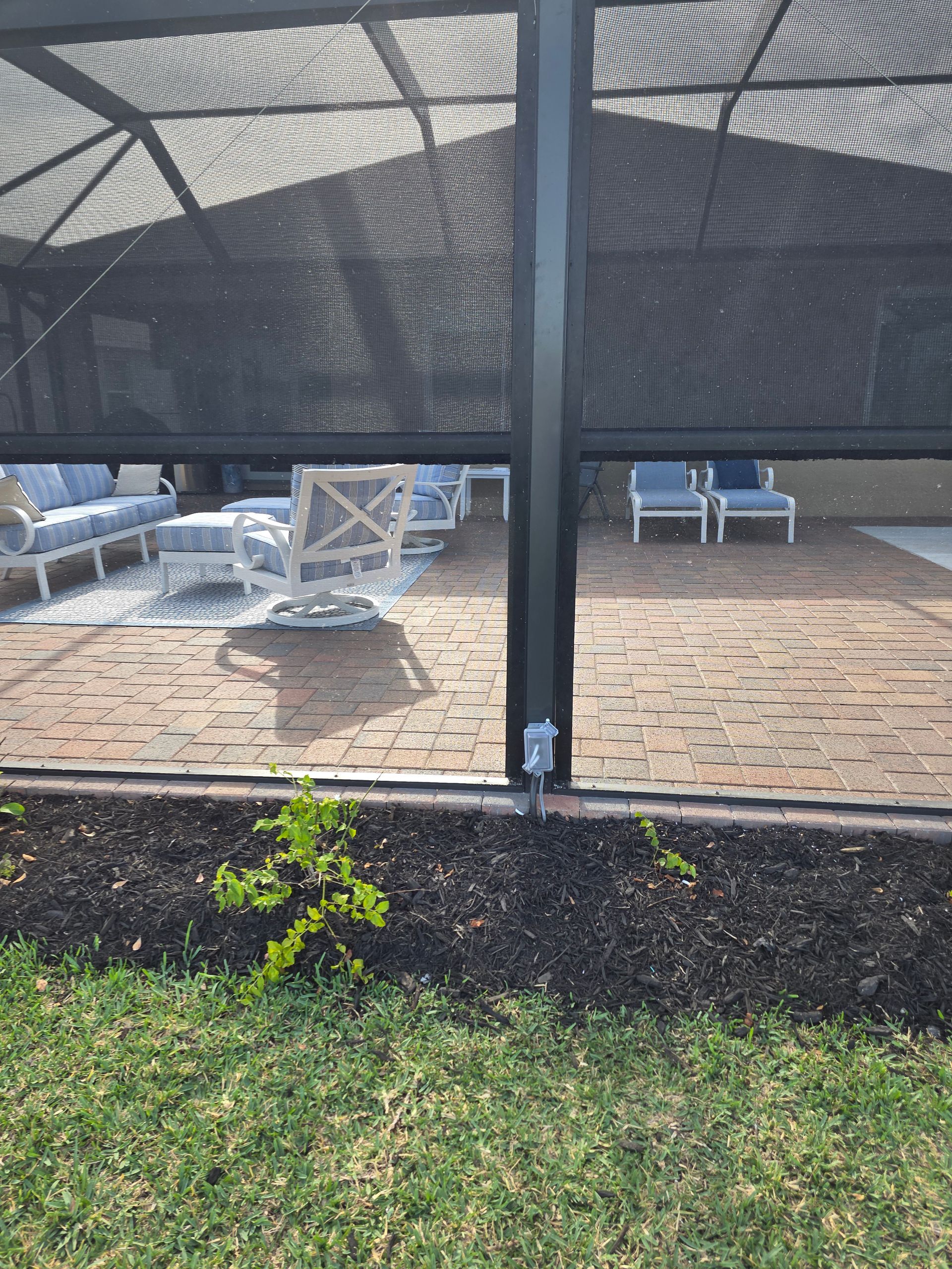 Screened patio with black mesh, brick pavers, outdoor furniture, and green lawn.