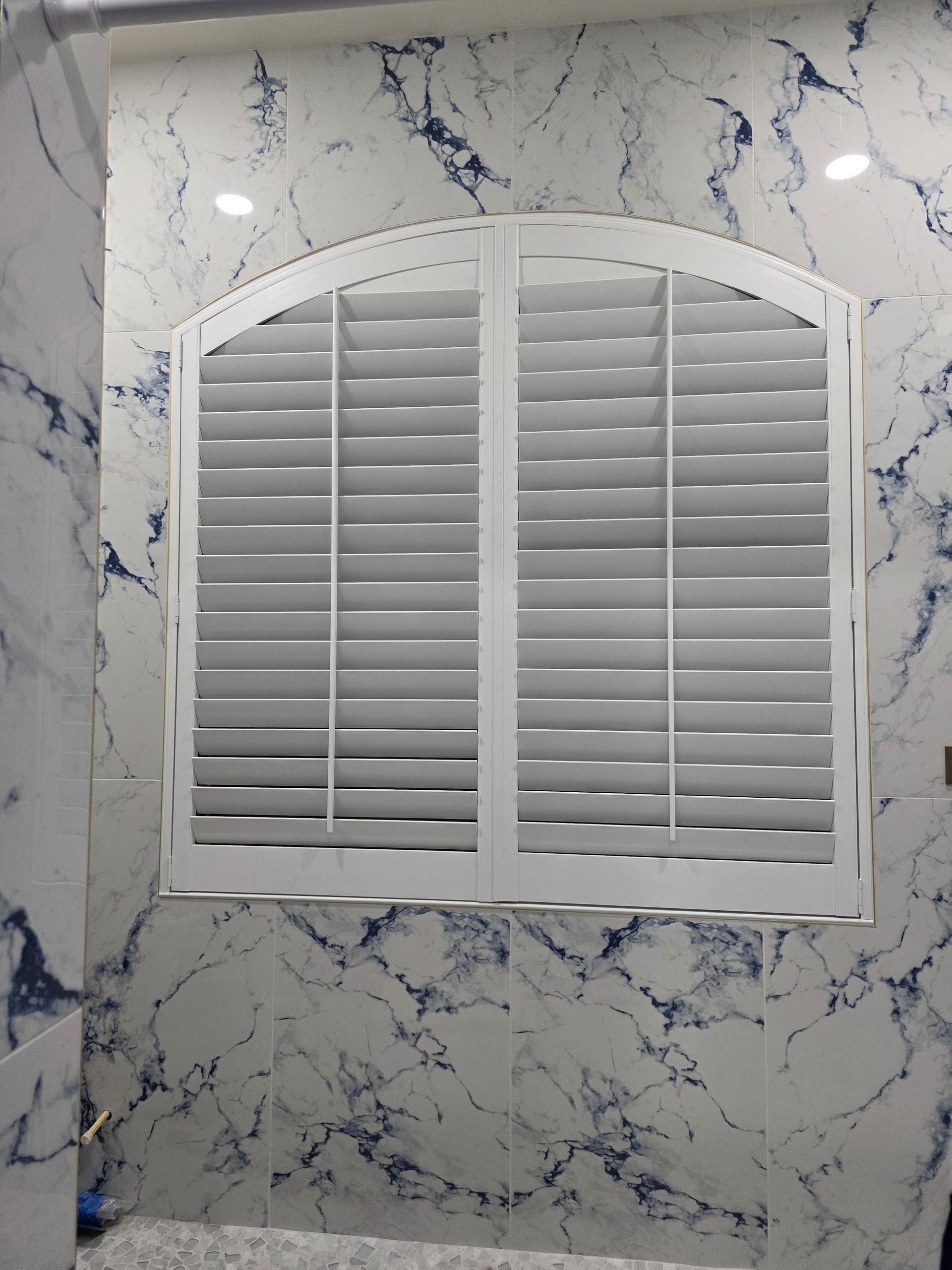 White arched window shutters on marble tile wall.