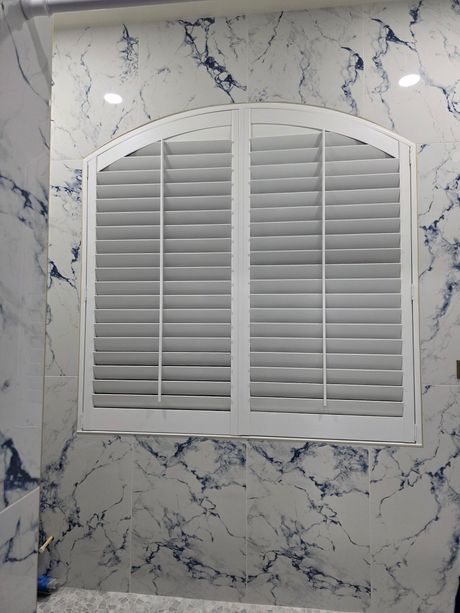 White arched window shutters on marble tile wall.