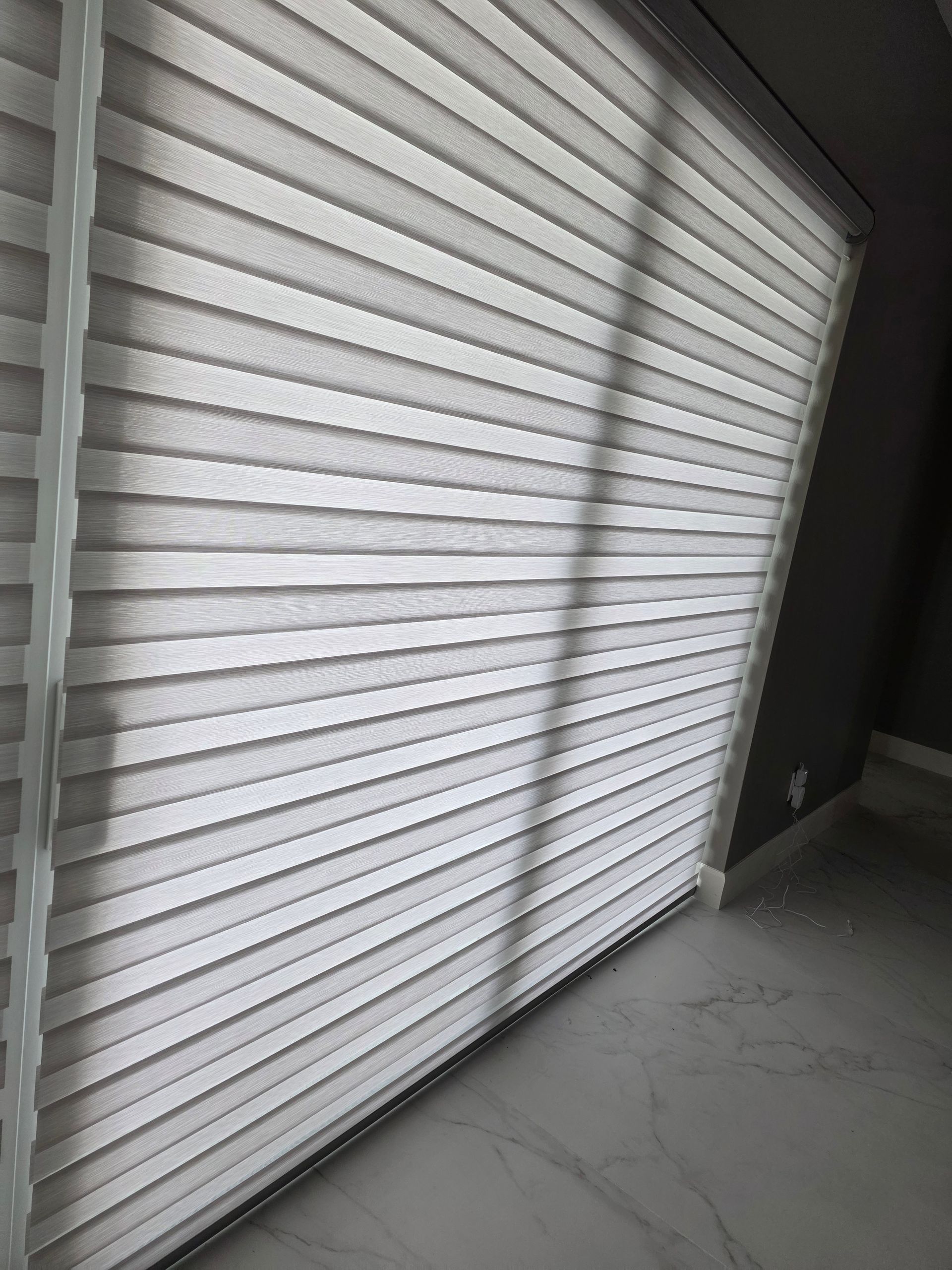 Window blinds, light and dark horizontal stripes, casting shadow on tiled floor.