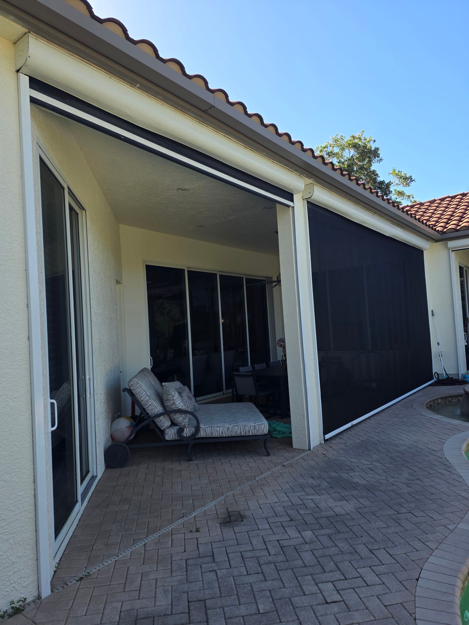 Patio with retractable black screen, stone flooring, and white exterior wall.