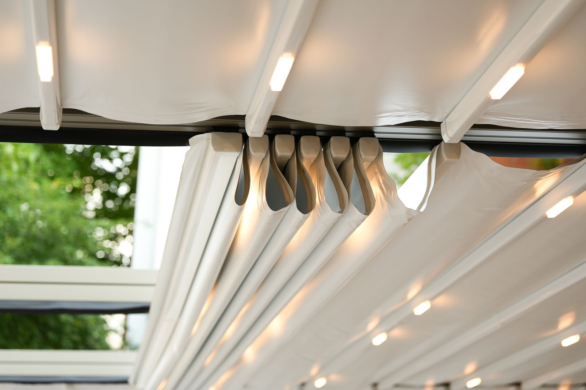 Close-up of a white retractable pergola roof with built-in lights, partially open, showing the mechanisms.