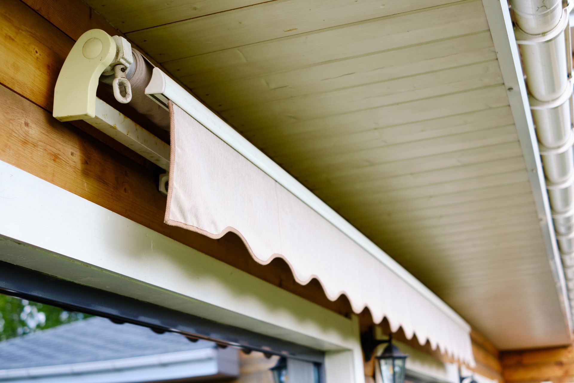 Beige retractable awning above a window on a wooden building.