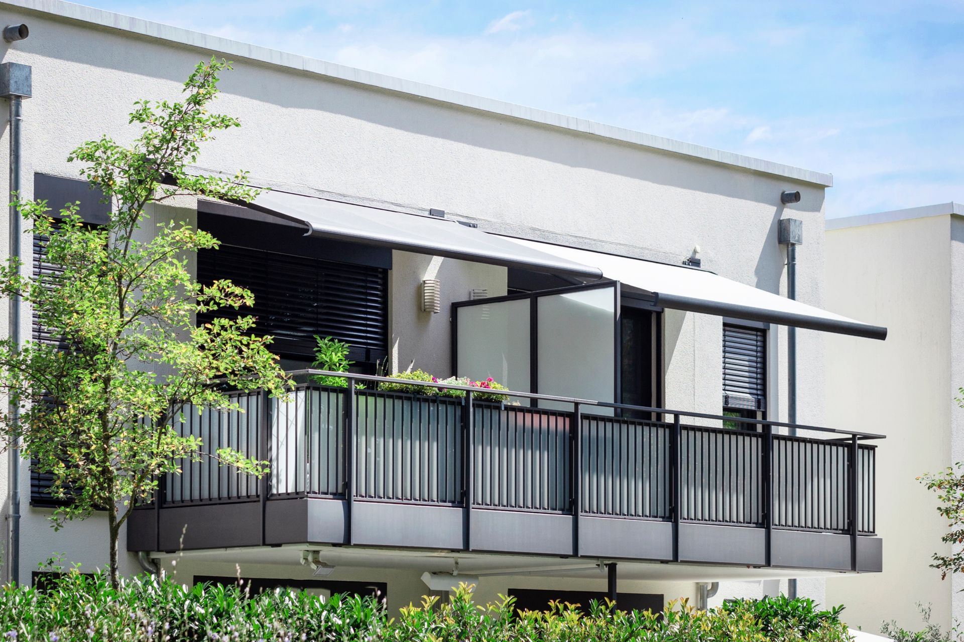 Balcony with awning, railing, and small plants on a modern white building exterior.