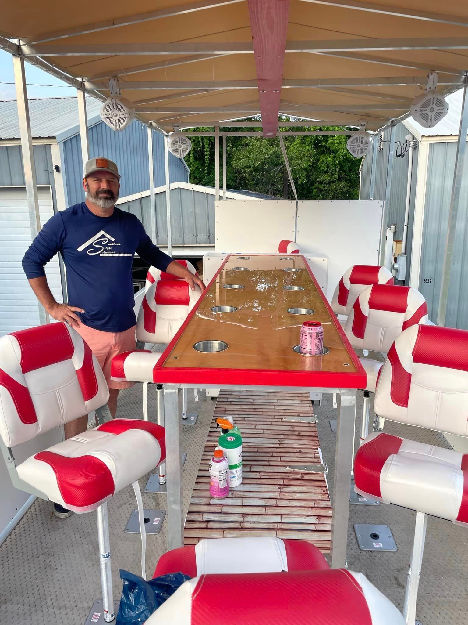 A man is standing next to a long table and chairs on a boat.