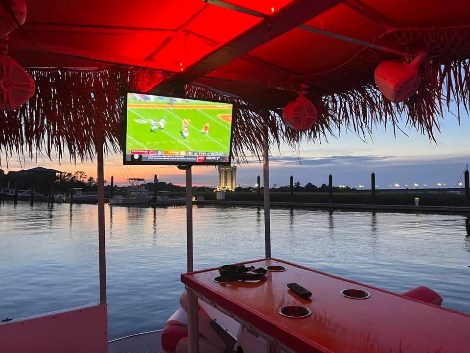 A large flat screen tv is hanging from the roof of a boat.