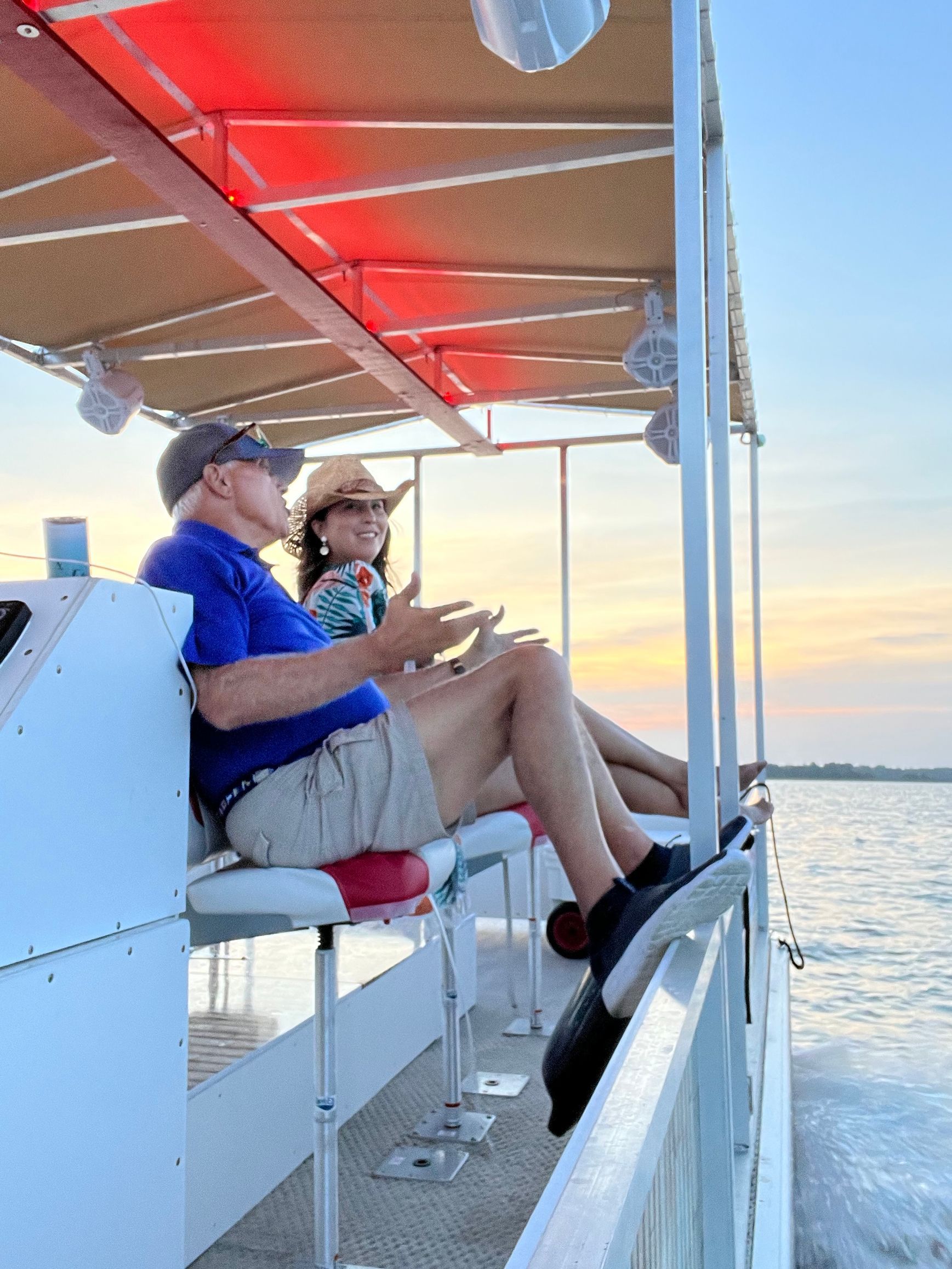 A man and a woman are sitting on a boat looking at the sunset.
