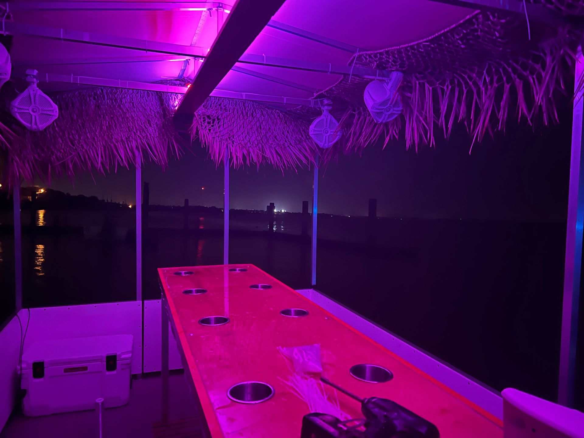 A long table with purple lights on it is on a boat at night.
