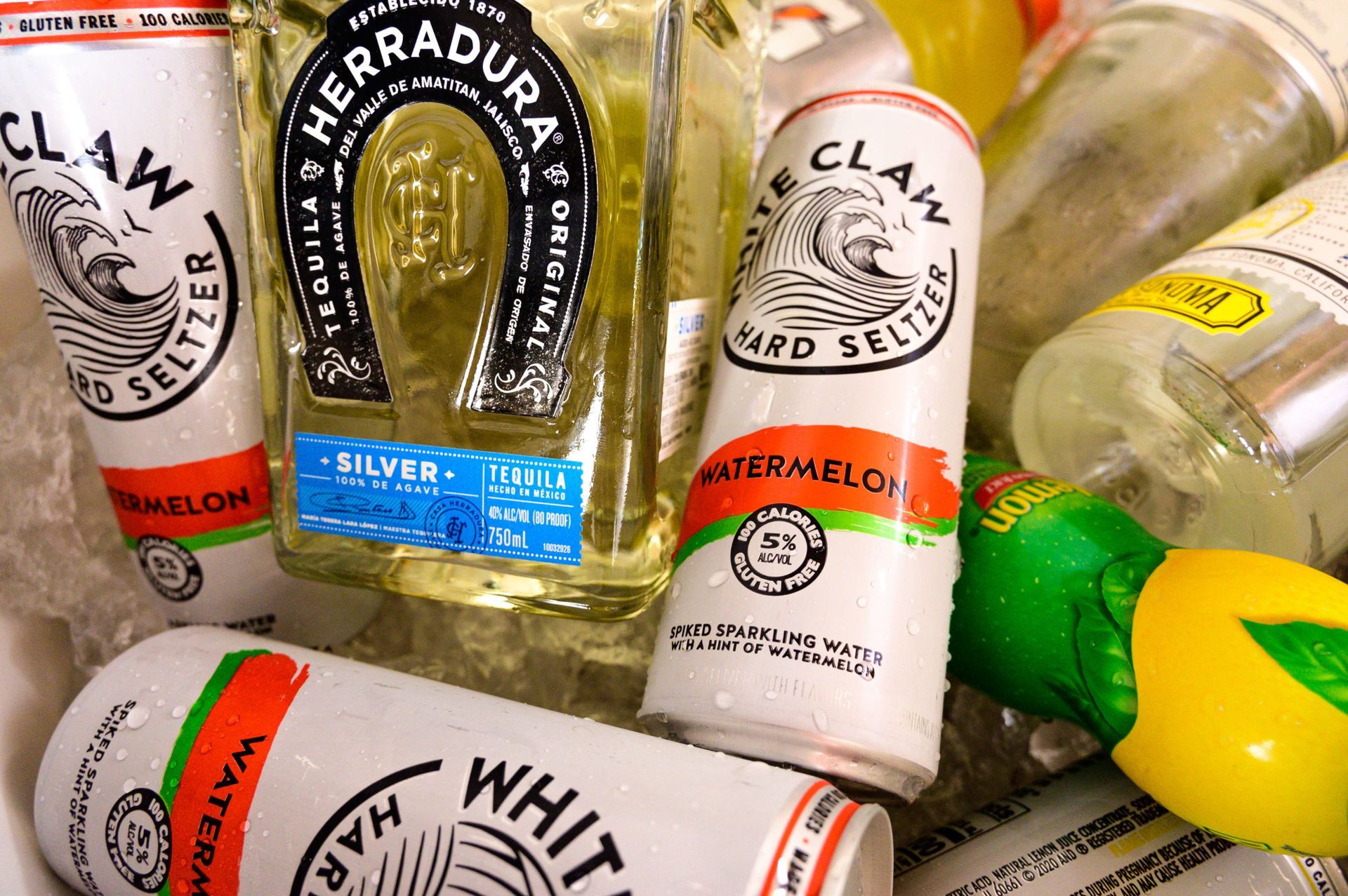 A bottle of herradura tequila surrounded by cans of watermelon and claw hard seltzer