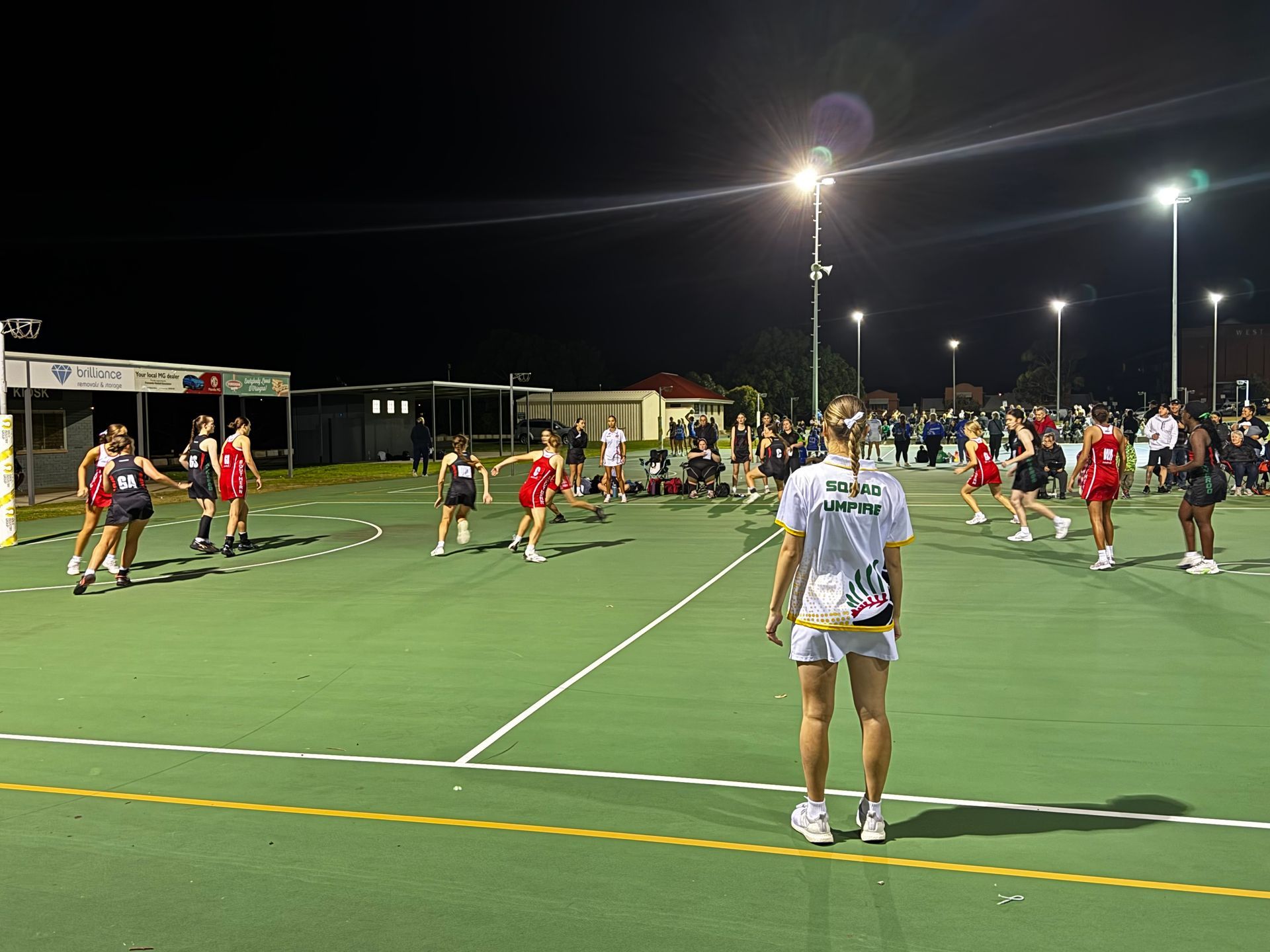 A group of people are playing netball on a court at night.