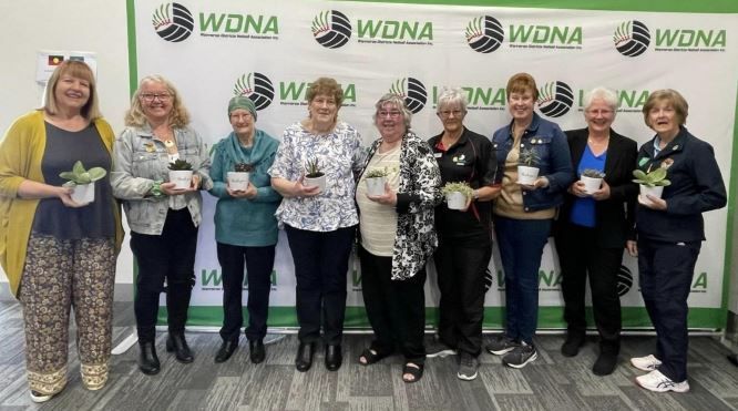 A group of women standing next to each other holding potted plants.