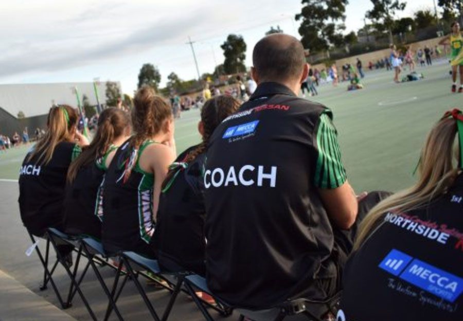 A group of people are sitting in a row wearing coach vests.