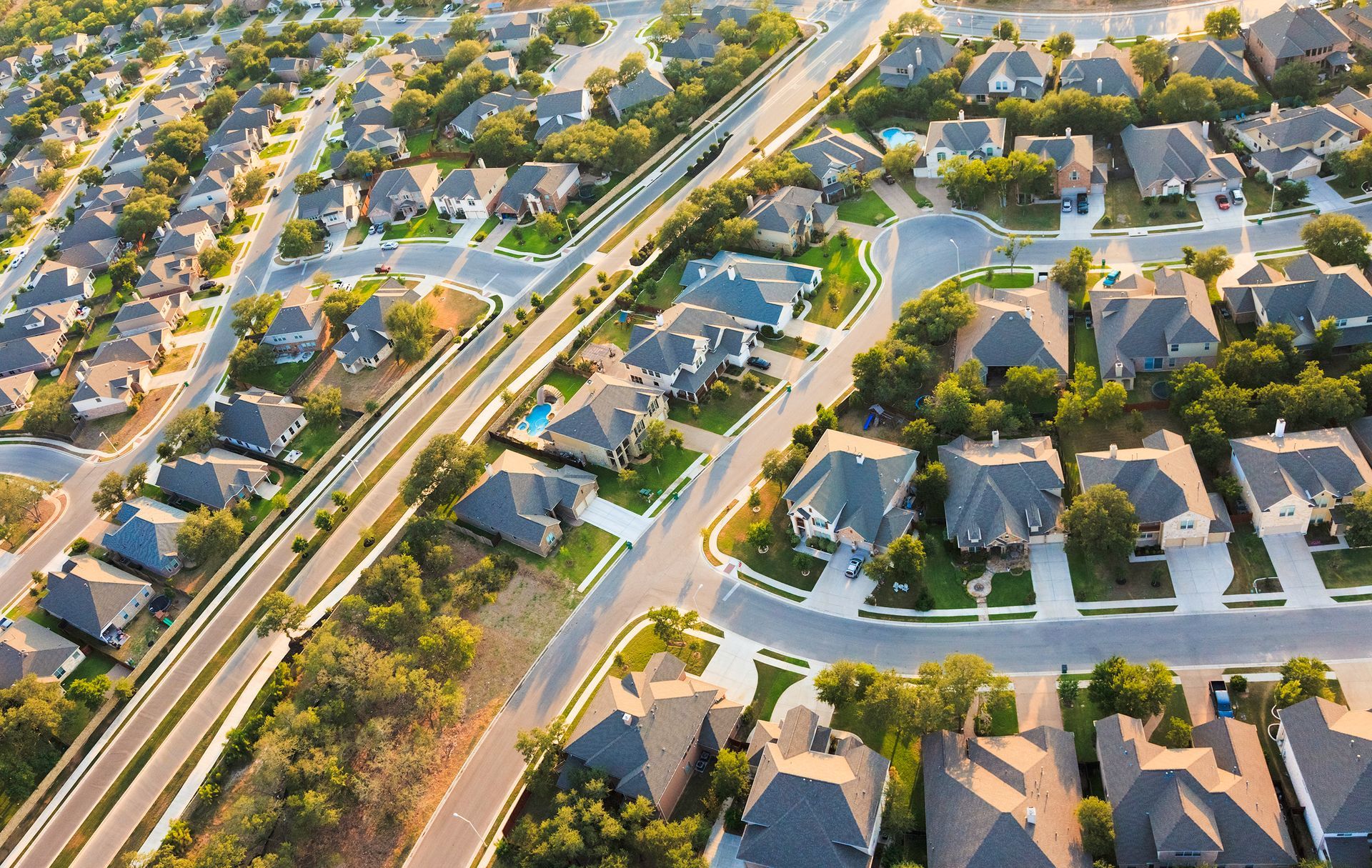 Aerial view of suburban homes with tree-lined streets, driveways, and a highway.