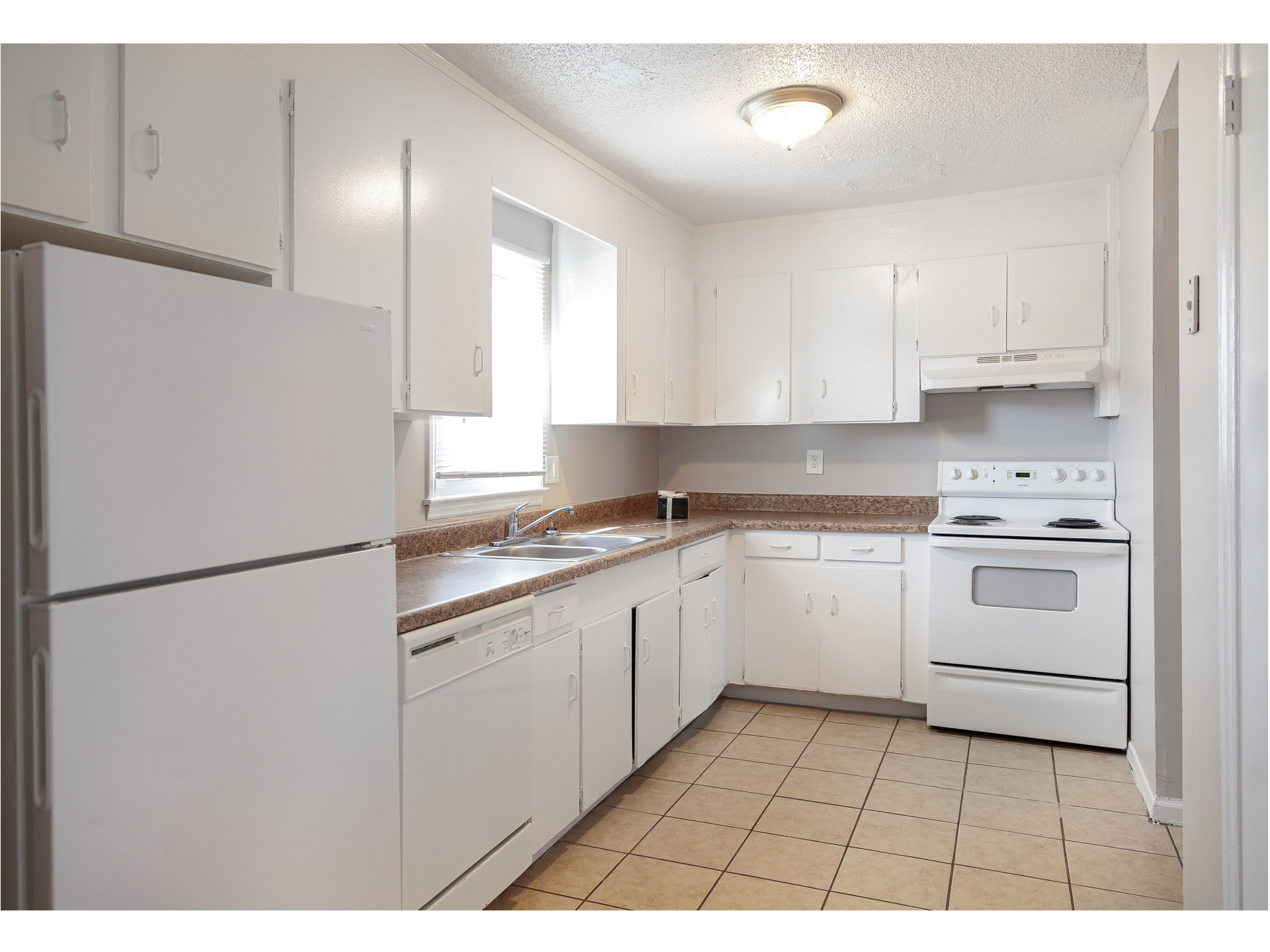 White kitchen with cabinets, sink, and stove in an apartment.