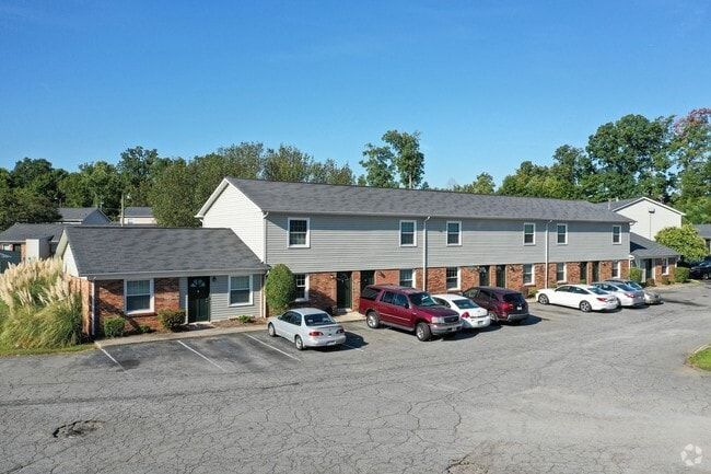 Apartment building exterior on a sunny day. Cars parked out front. Gray siding, brick accents.