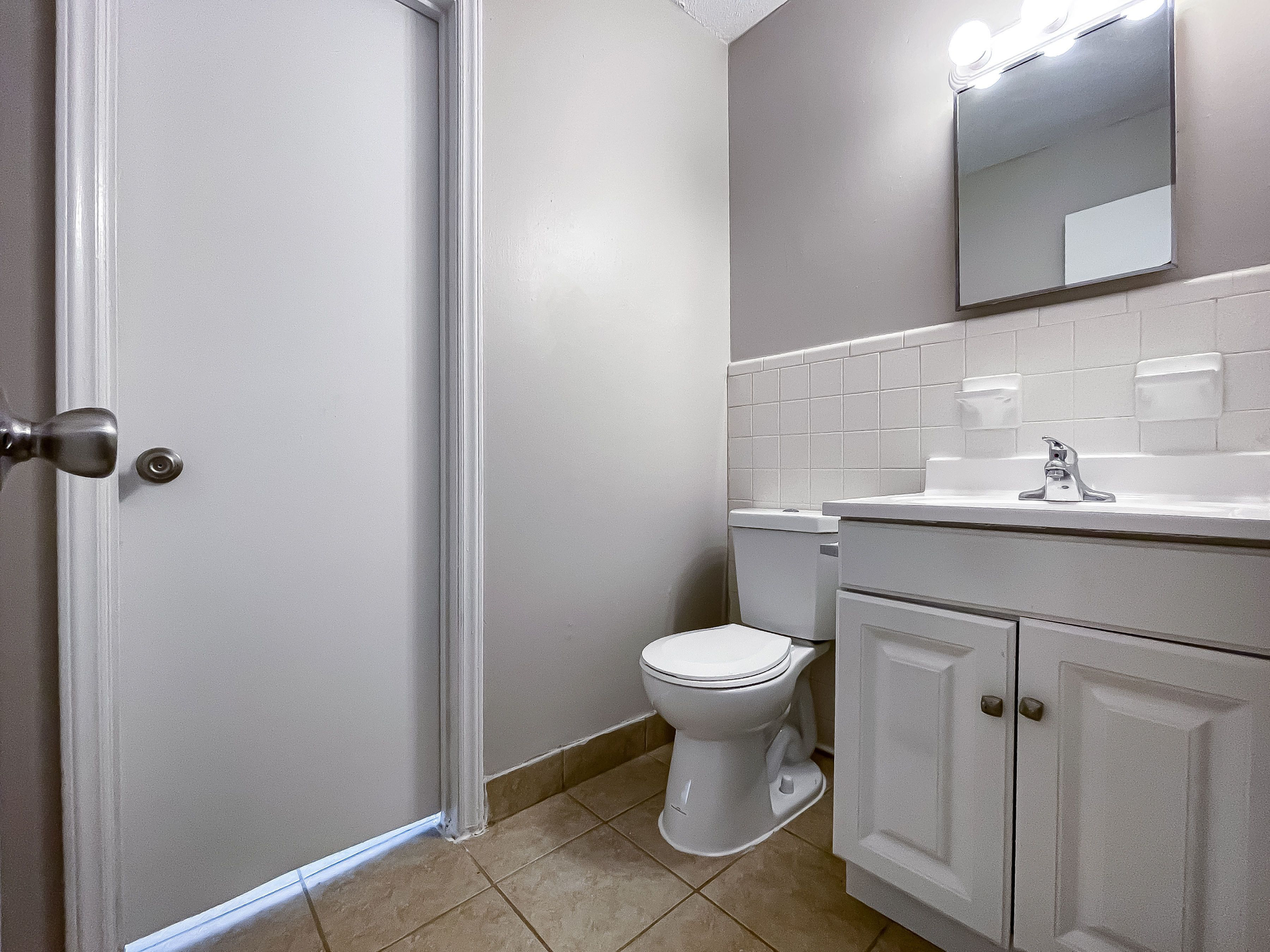 Bathroom in an apartment: white vanity with sink, toilet, mirror, and tiled floor.