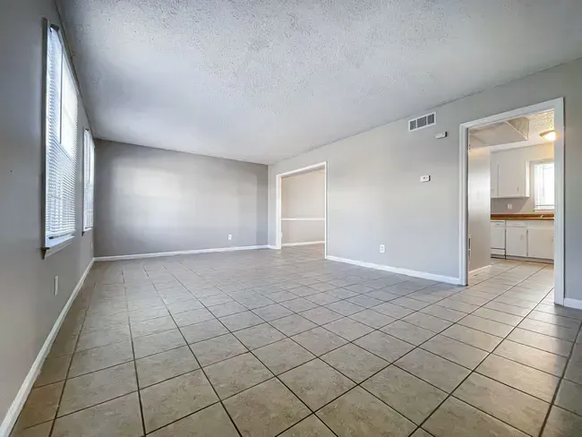 Empty living room with gray walls, tiled floor, and doorway to kitchen.