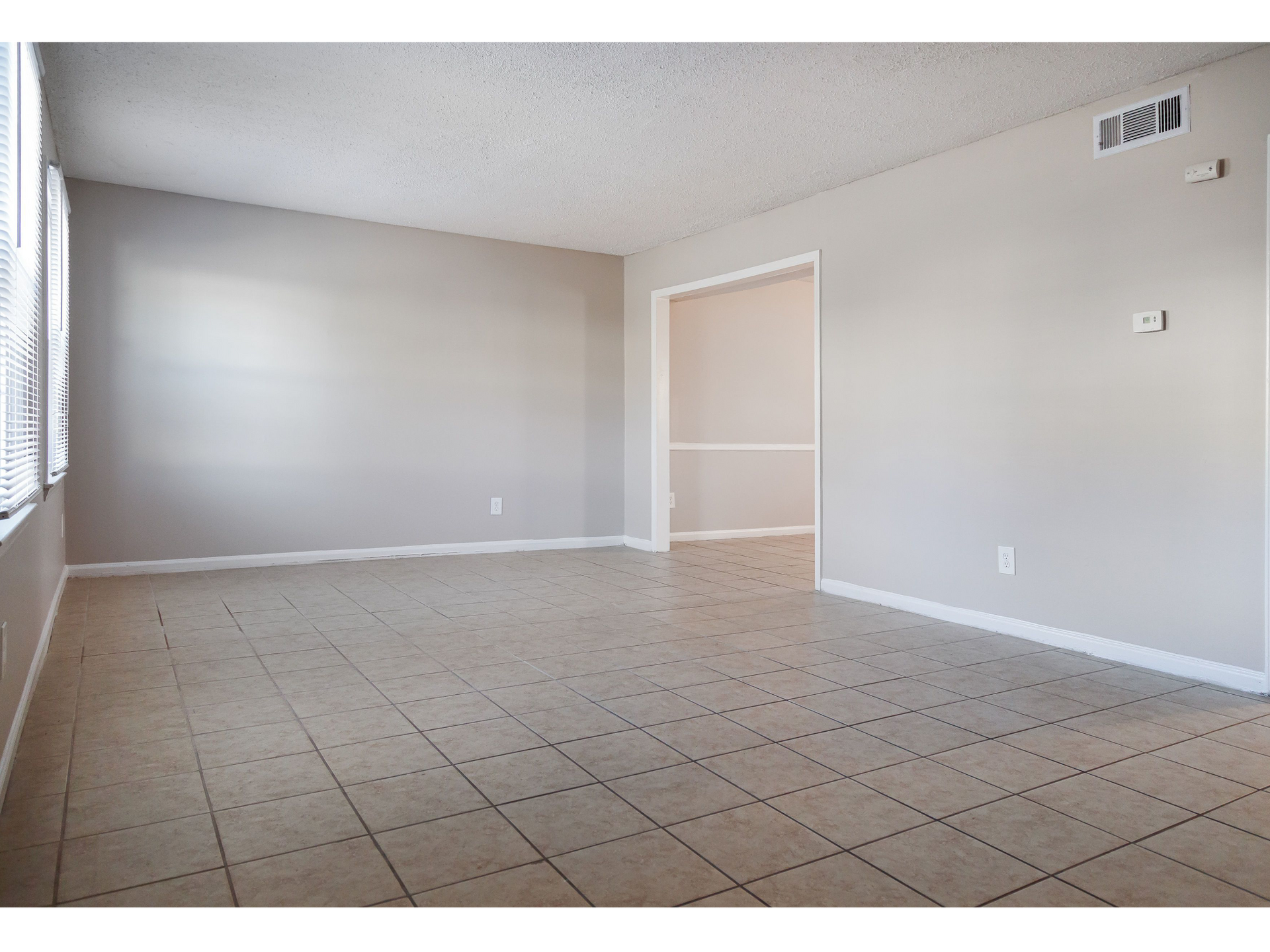 Empty apartment living area with tiled floor, gray walls, and a doorway to another room.