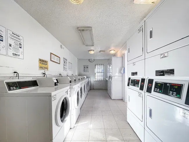Laundry room with rows of white washers and dryers; bright, clean space.