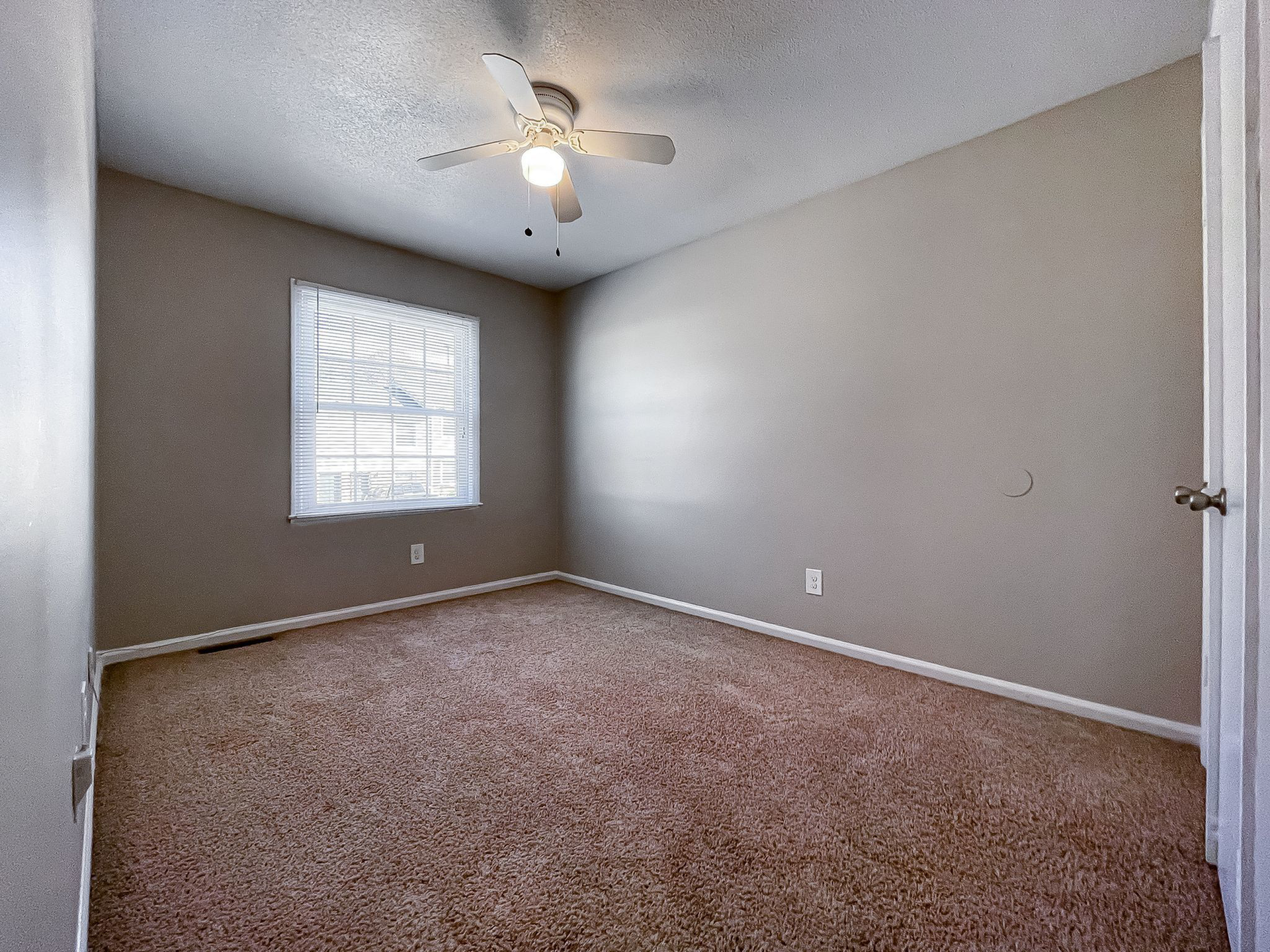 Empty beige bedroom with a window, carpet, and a ceiling fan.