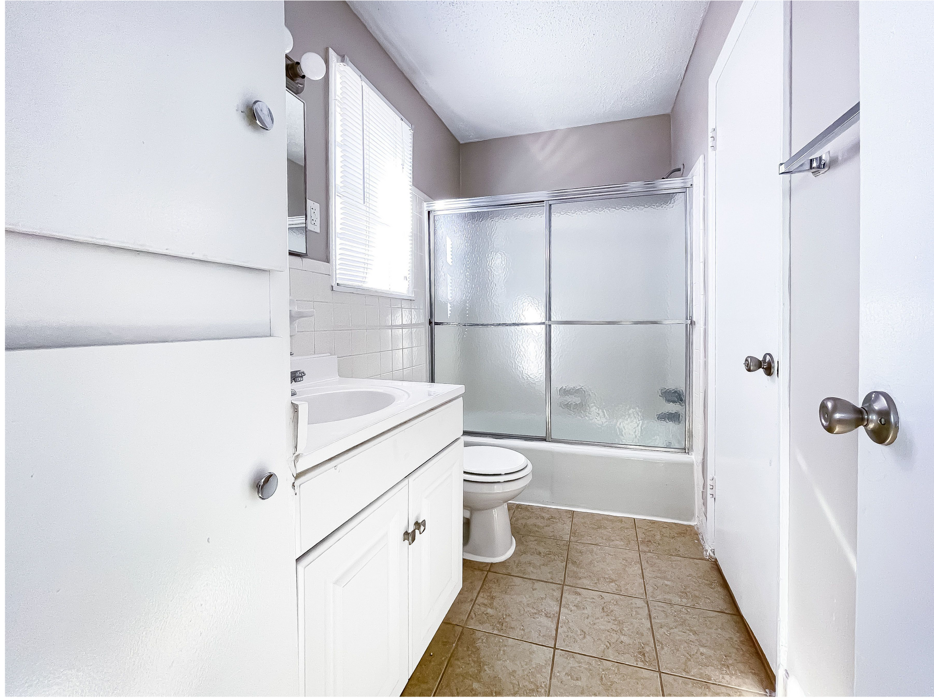 White bathroom with a vanity, sink, toilet, and frosted glass shower doors.