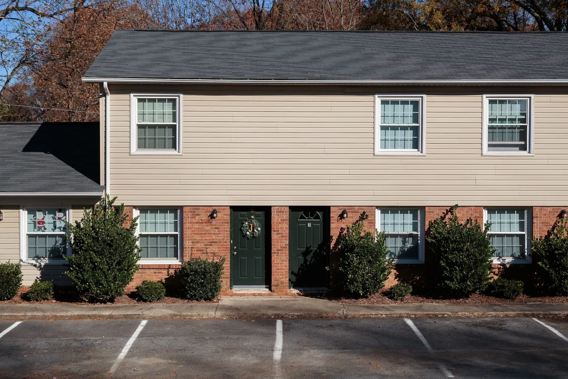 Exterior of a two-story beige apartment building with brick base and landscaped shrubs.
