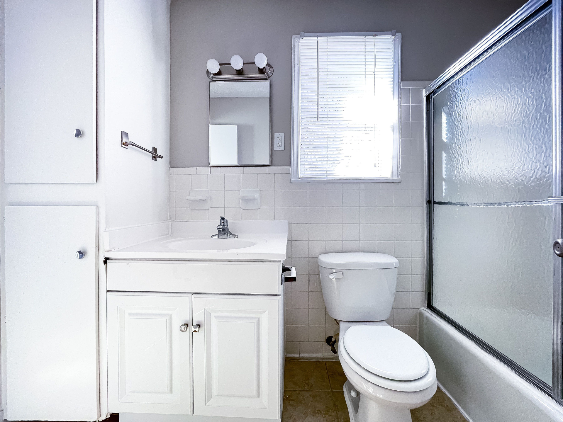 White bathroom with vanity, sink, mirror, toilet, and sliding glass shower.