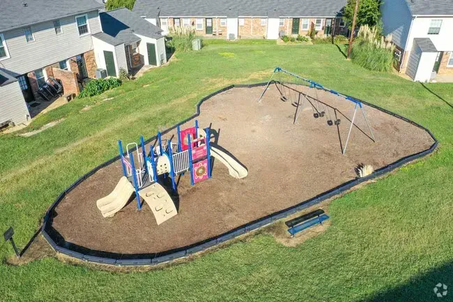 Playground with swings and slide in front of a low-rise apartment building on a sunny day.