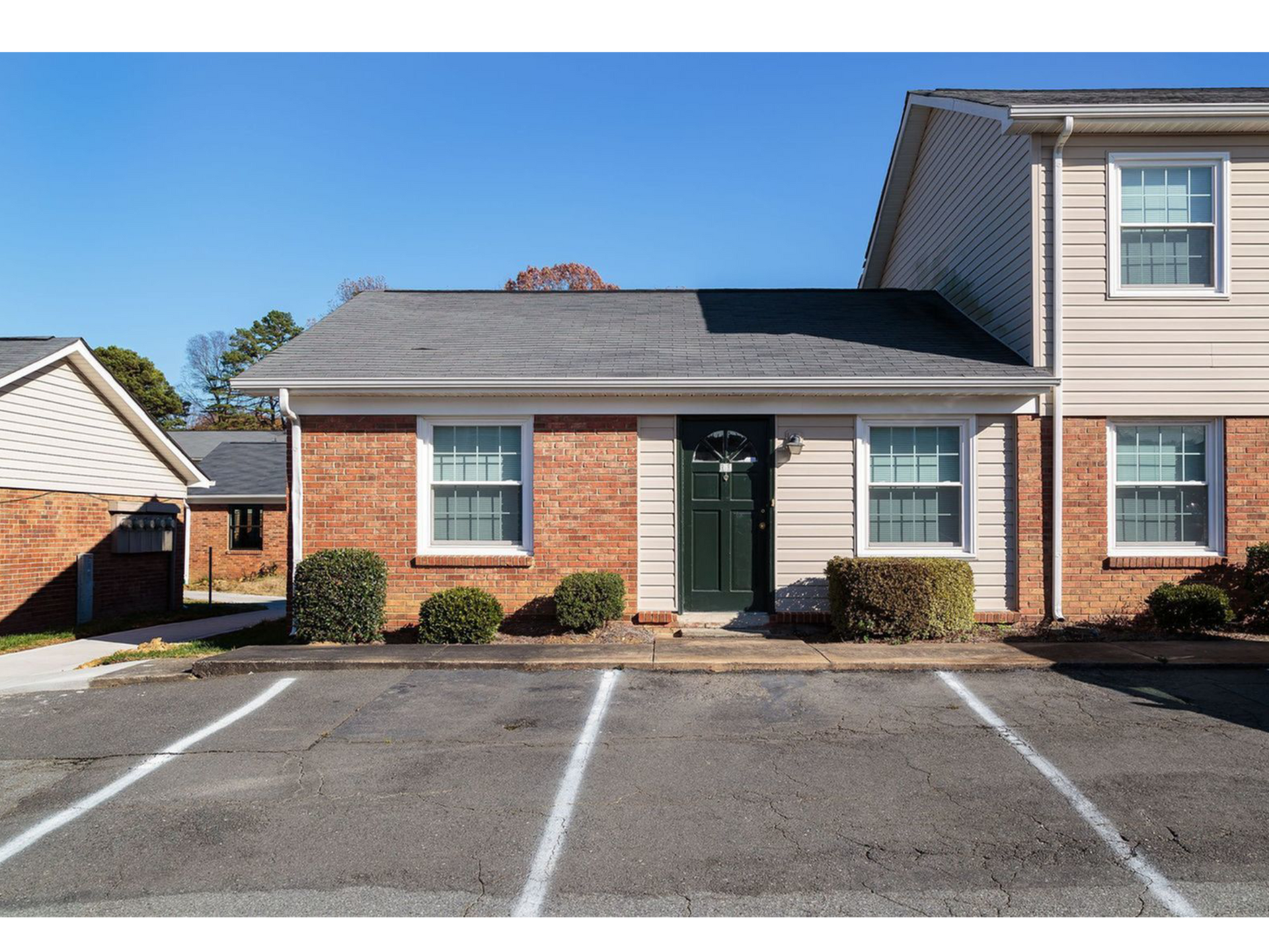 Exterior of a brick apartment building with a green front door and front parking.