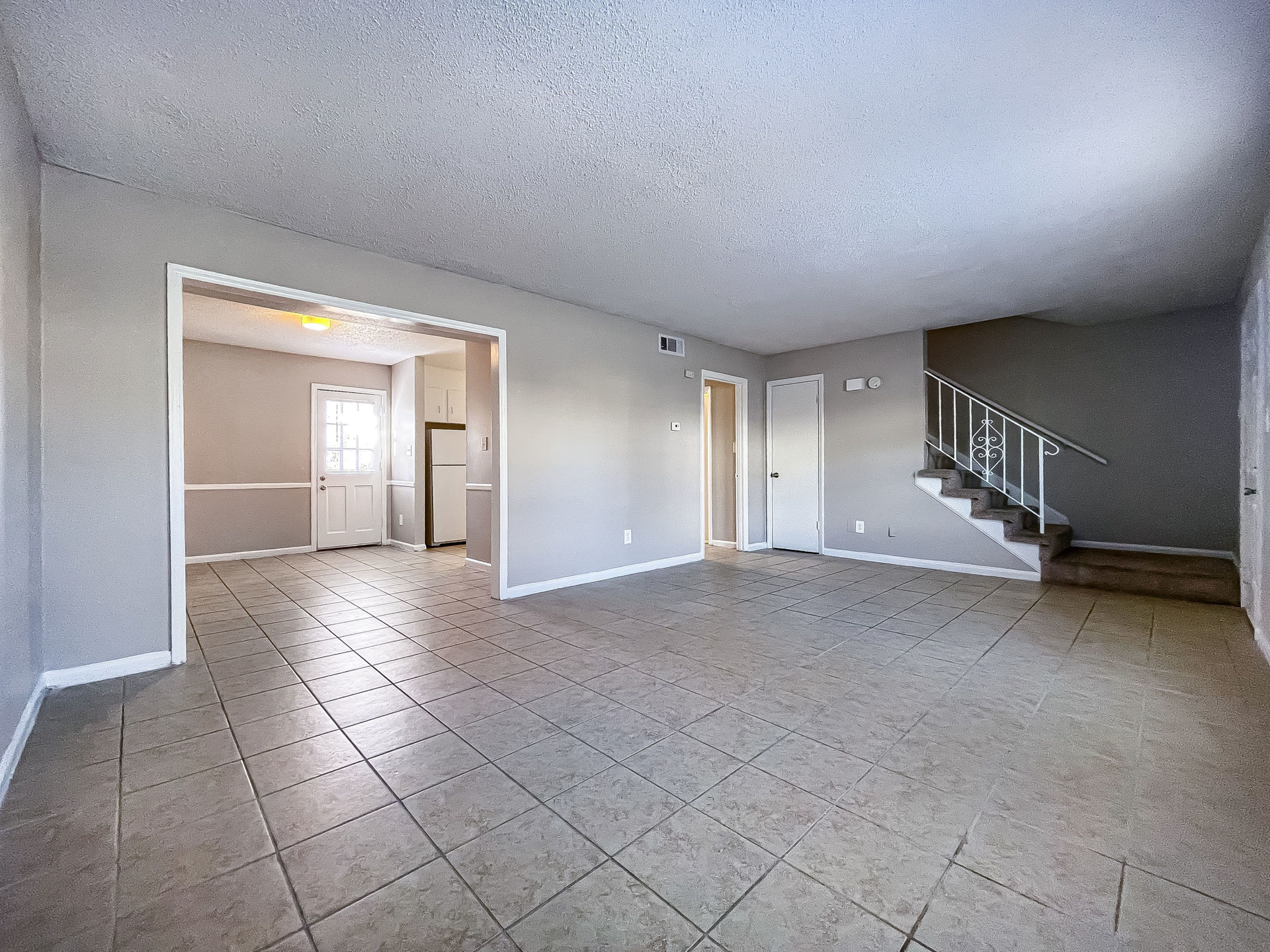 Living room with tiled floor, gray walls, a staircase railing, and a doorway to the kitchen.