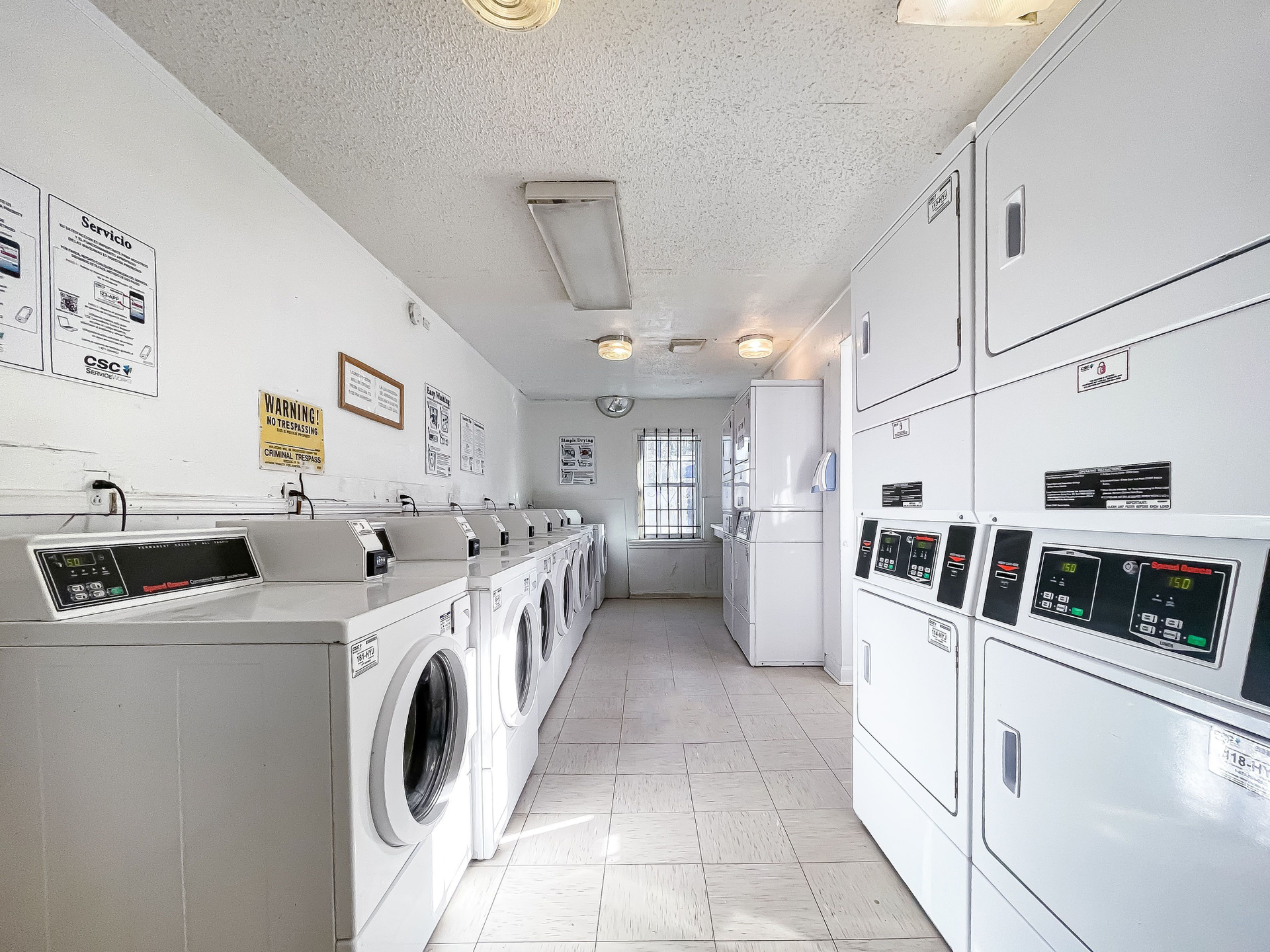 Community laundry room with a row of white washing machines and stacked dryers along white walls.